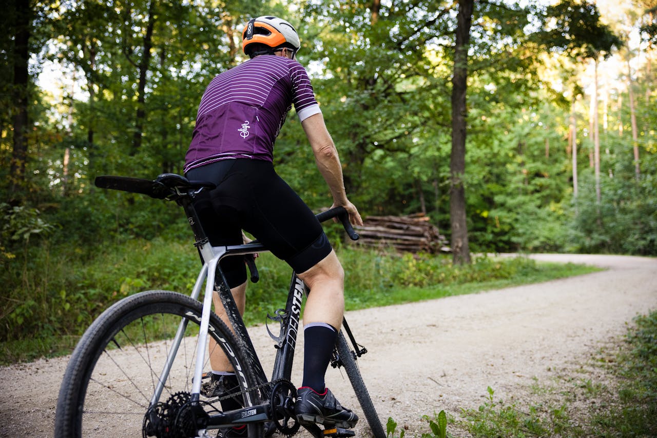 our-journey-01 A cyclist wearing a helmet rides a road bike through a lush green forest trail.